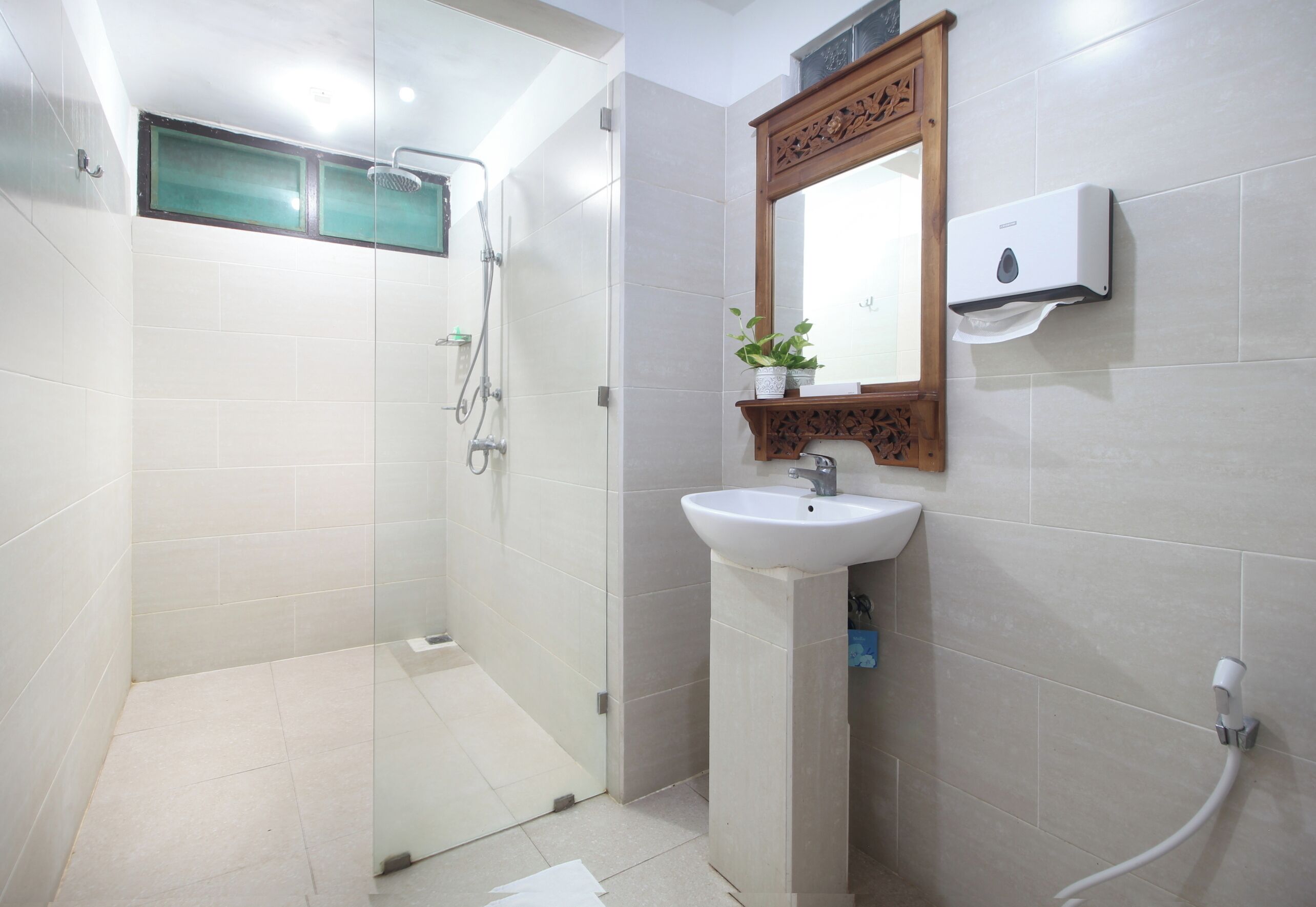 Un baño con ducha envuelta en vidrio, un lavamanos con espejo y dispensador de jabón en la pared.