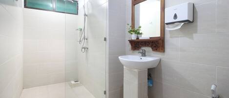 Un baño con ducha envuelta en vidrio, un lavamanos con espejo y dispensador de jabón en la pared.