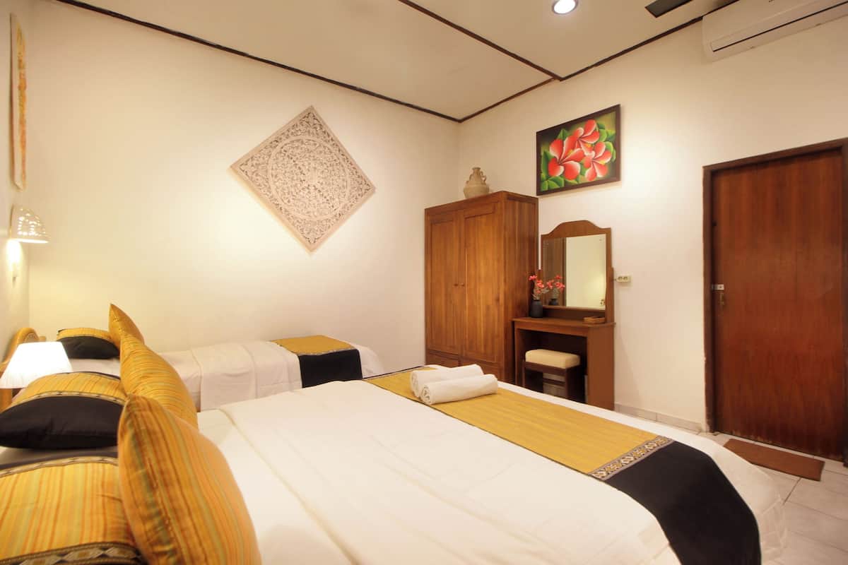 A hotel room with two beds, a wooden wardrobe, a mirror, and a door.