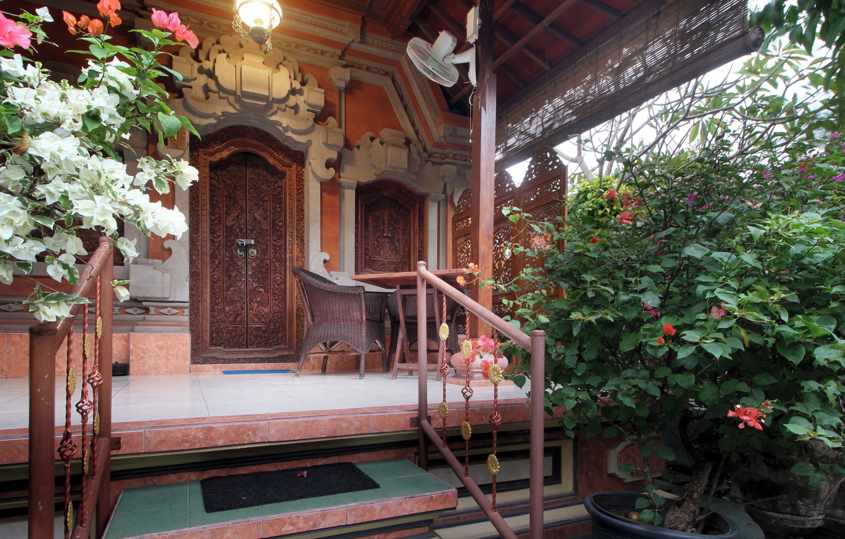 A traditional wooden building with intricate carvings, a covered porch, and a potted plant with flowers.