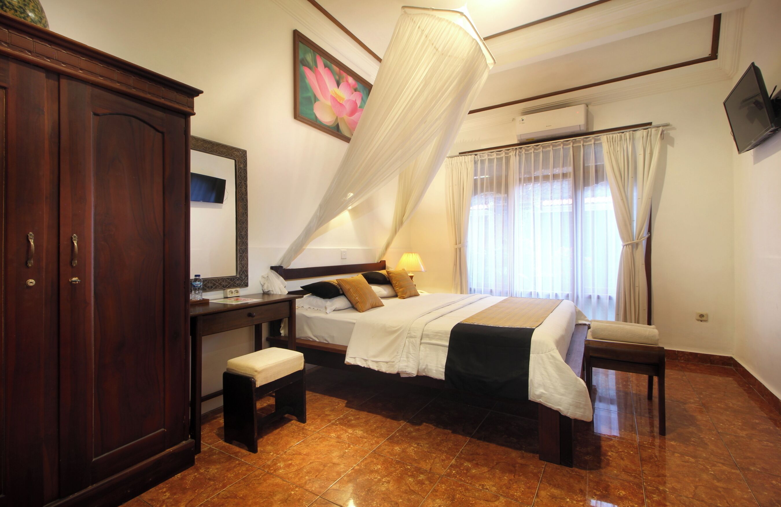 A bedroom with a bed, bedside table, bench, wardrobe, and a large mirror.