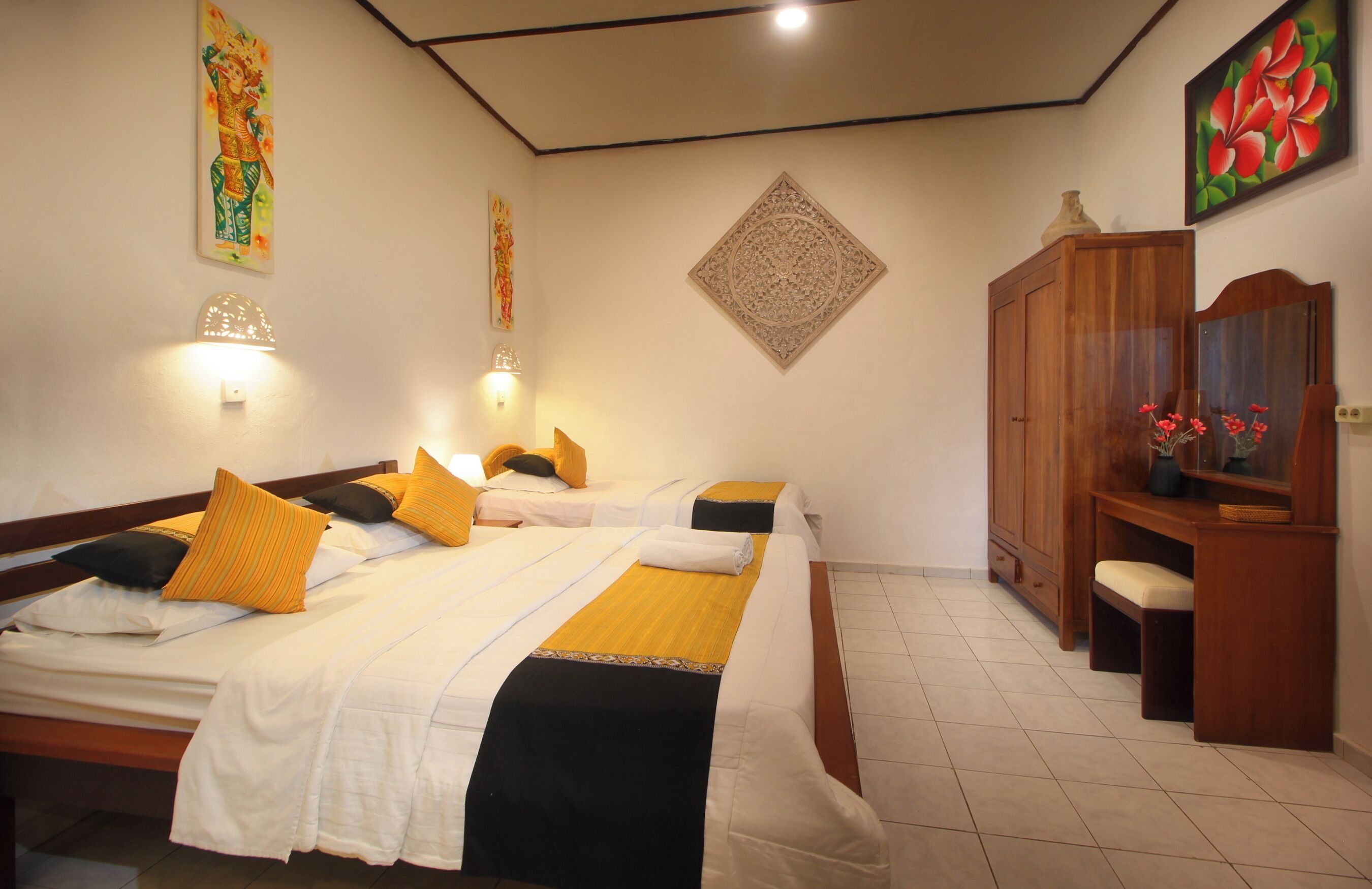 A hotel room with two beds, a wooden wardrobe, and a small desk with a mirror.