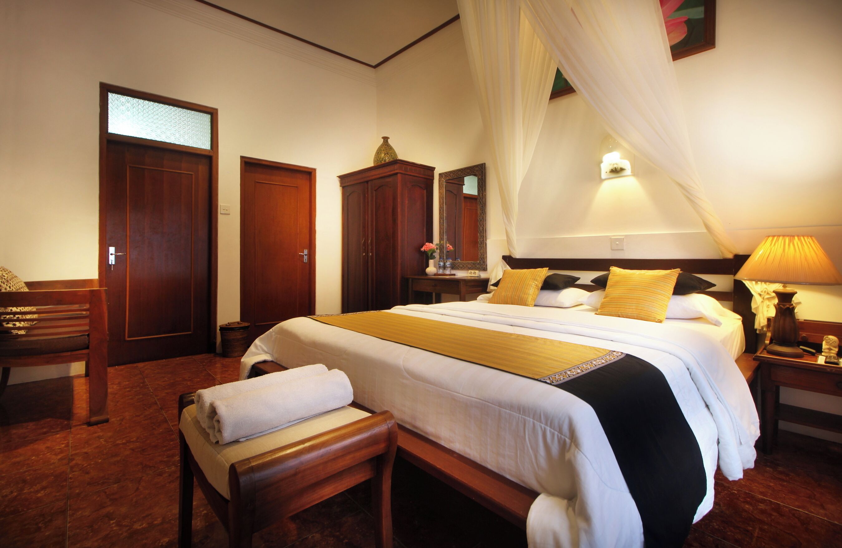 A well-lit bedroom with a large bed, a bedside table, a bench, and a wardrobe.