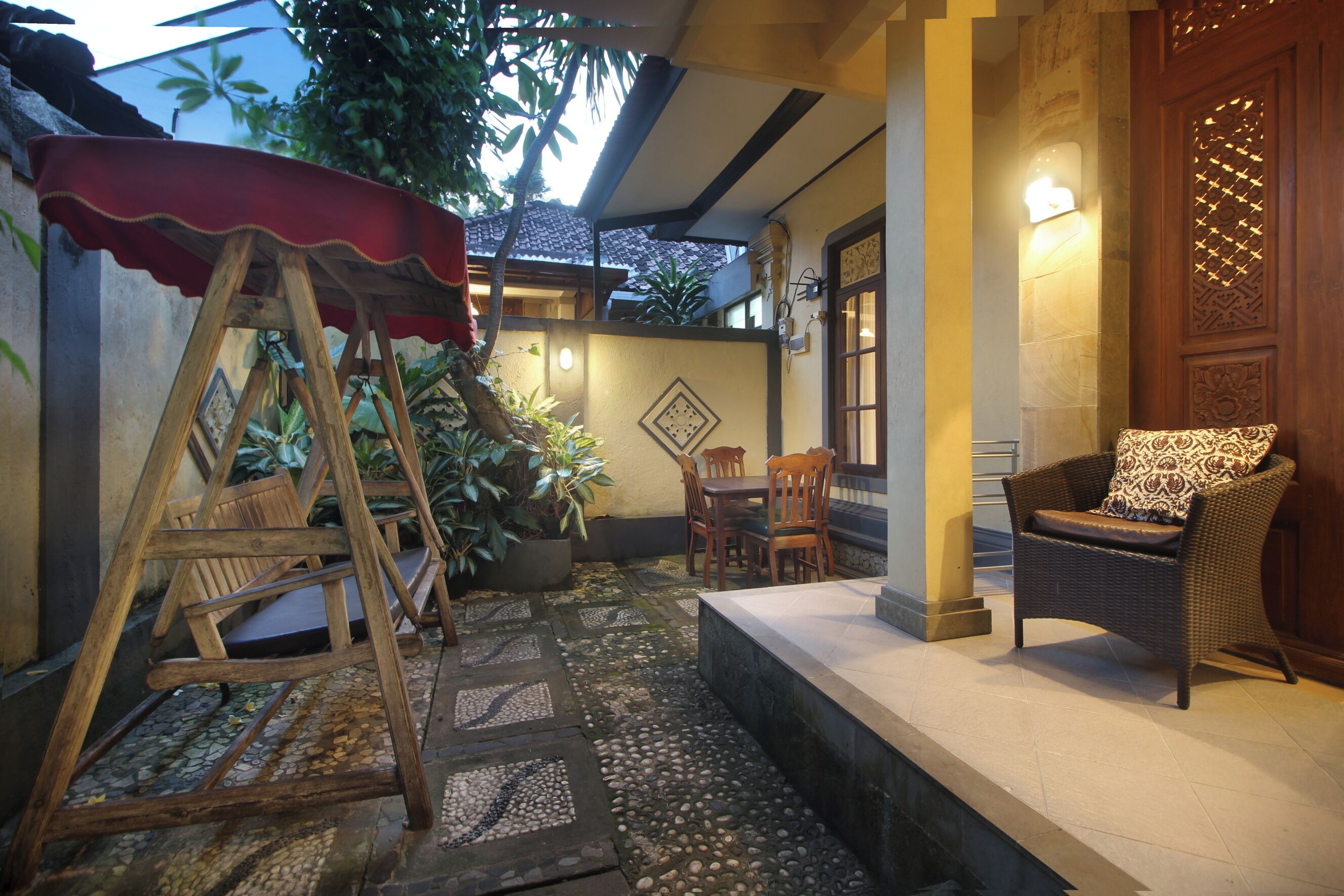 Uma área de estar externa aconchegante com mesa e cadeiras de madeira, um sofá de vime e um guarda-sol vermelho.