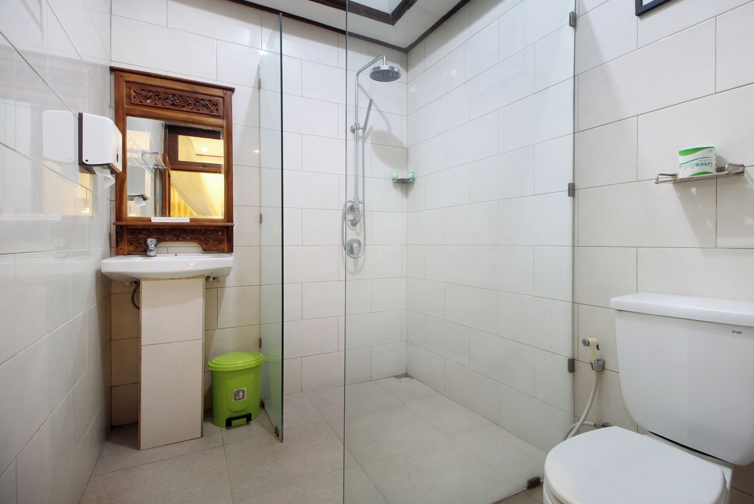 A bathroom with a toilet, sink, shower, and a green trash bin.