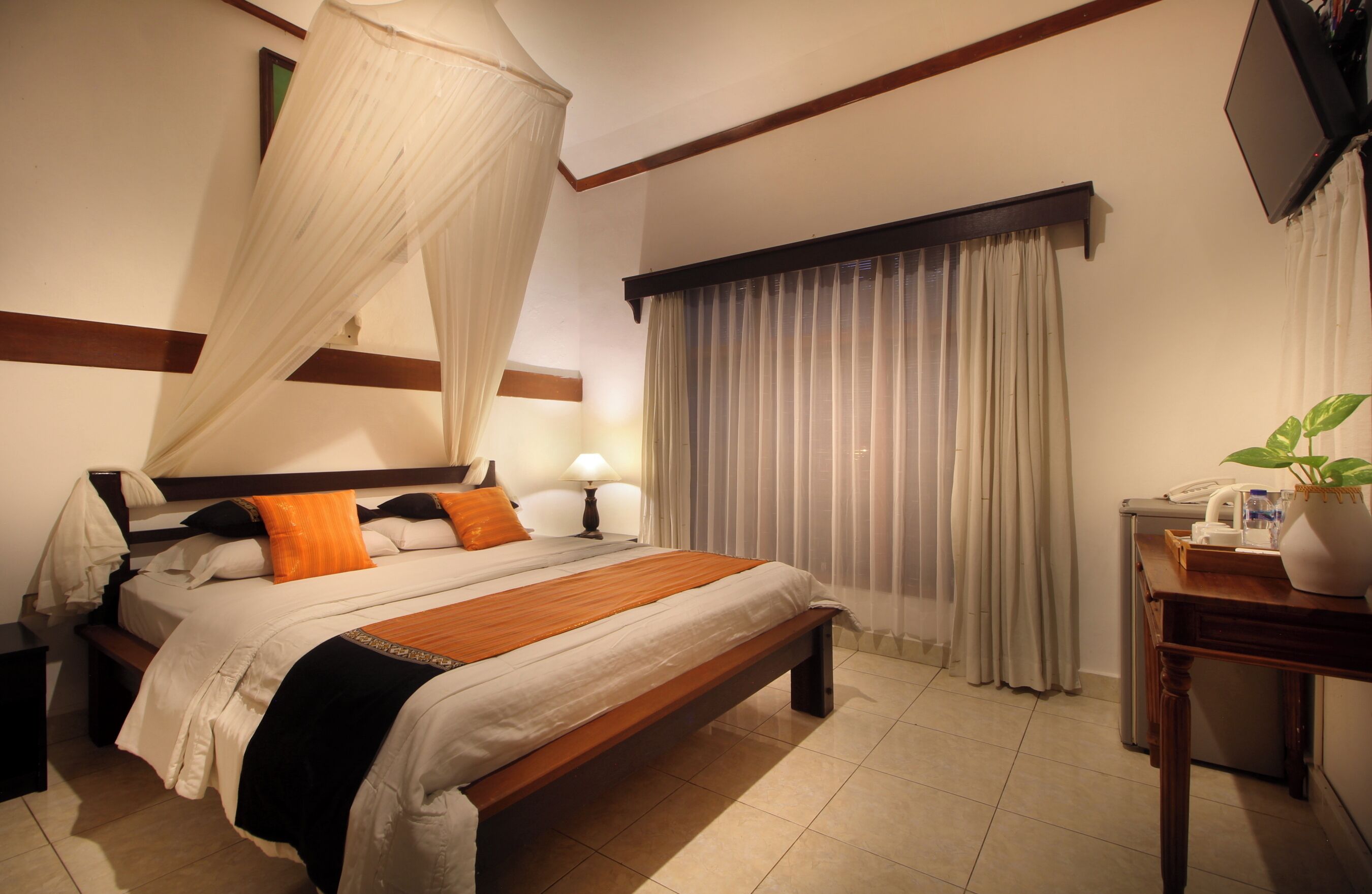 A hotel room with a large bed, a bedside table, a lamp, a TV, and a window with curtains.