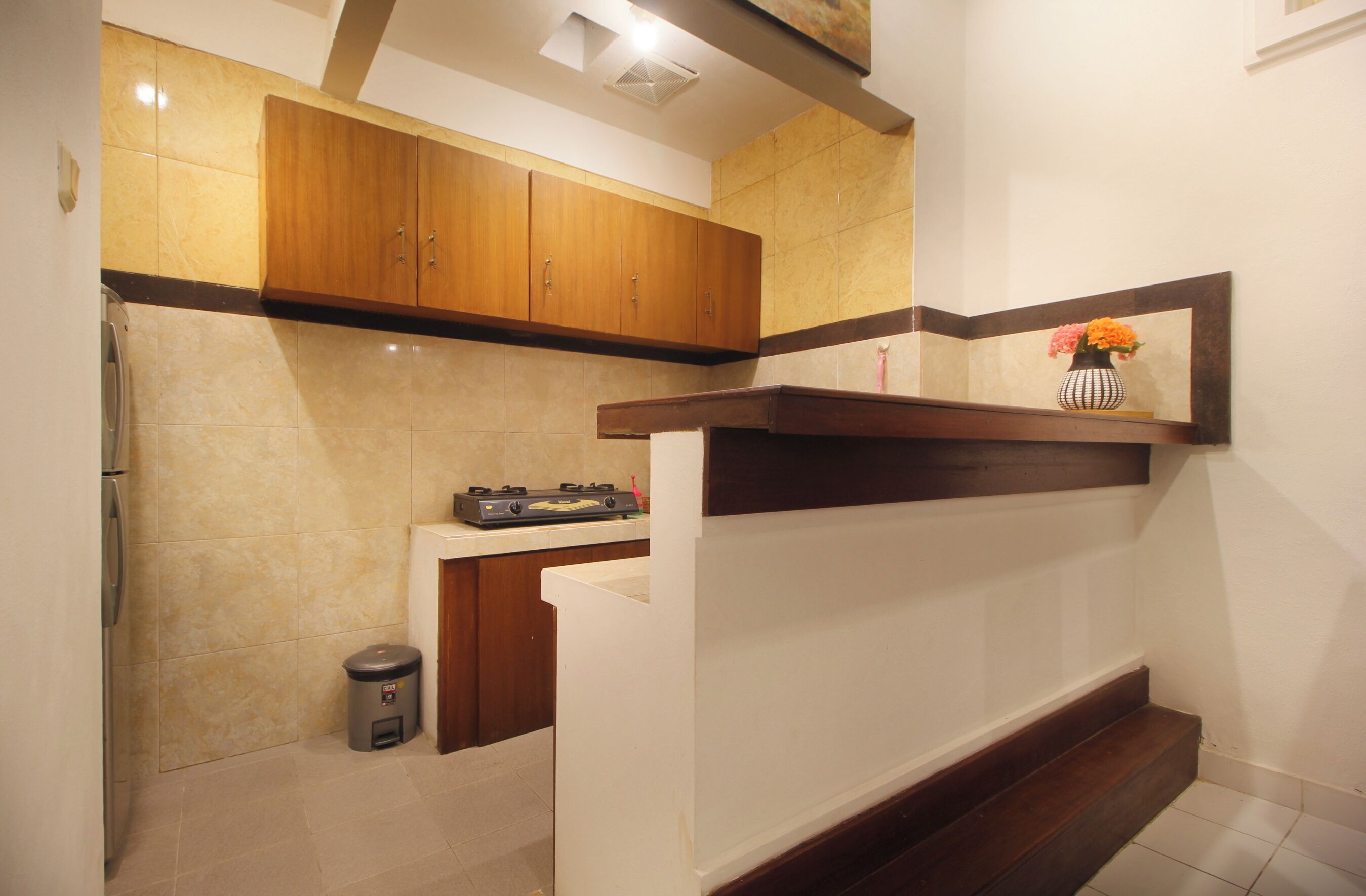 A kitchen with wooden cabinets, a countertop with a gas stove, and a trash can.
