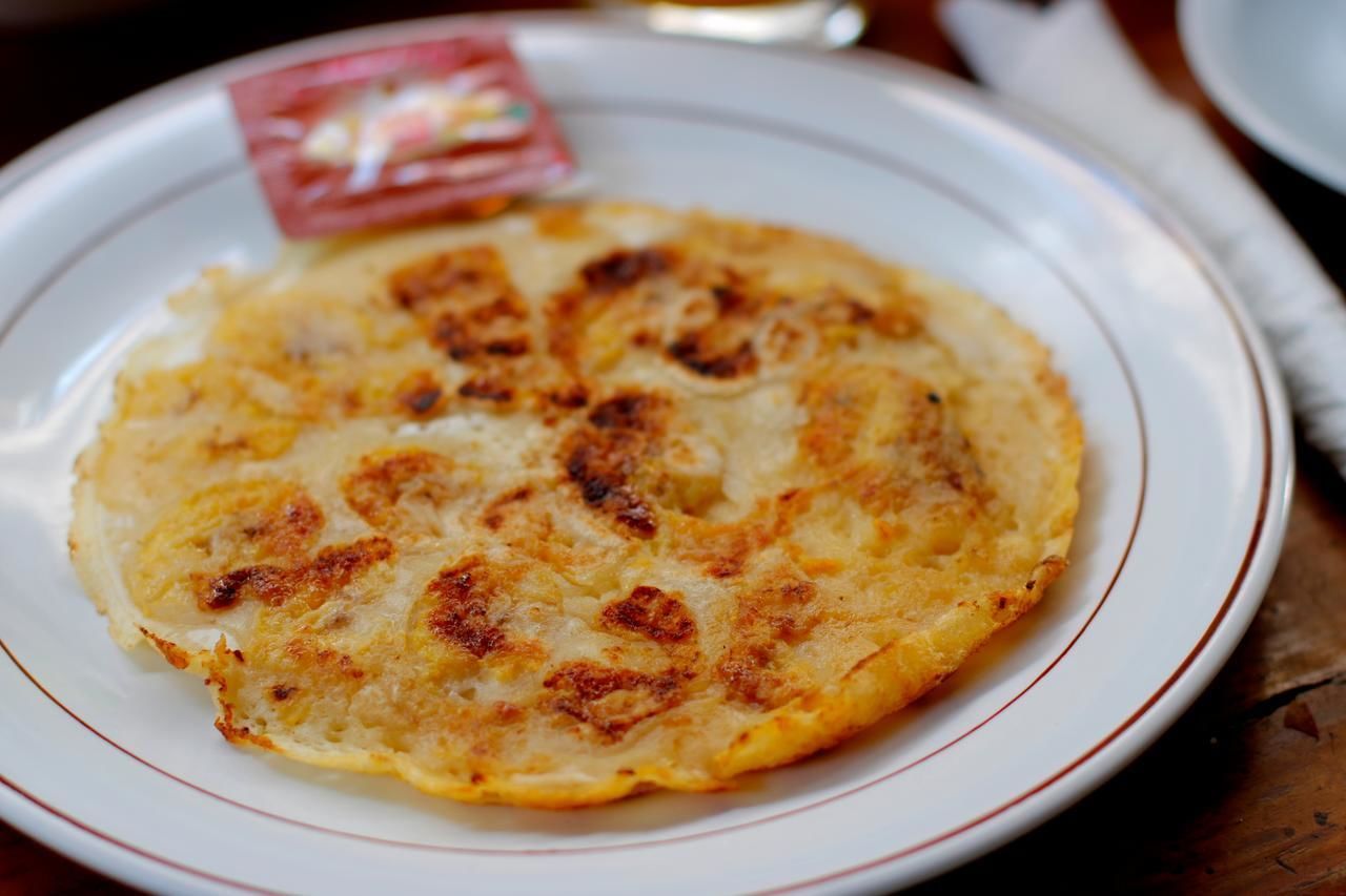 A plate with a golden-brown pancake on a white plate with a red rim.