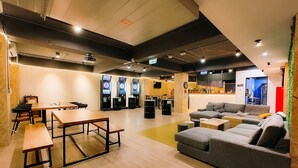 Un espace de détente moderne avec un plancher en bois, un canapé gris, une table en bois et un jeu de fléchettes.
