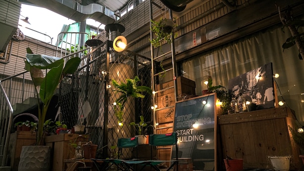 Un espace extérieur accueillant, aménagé avec des chaises et des plantes en pot, une clôture en bois et un panneau sur lequel on peut lire : « ARRÊTEZ DE FAIRE DES CROQUIS, PASSEZ À L’ACTION ».