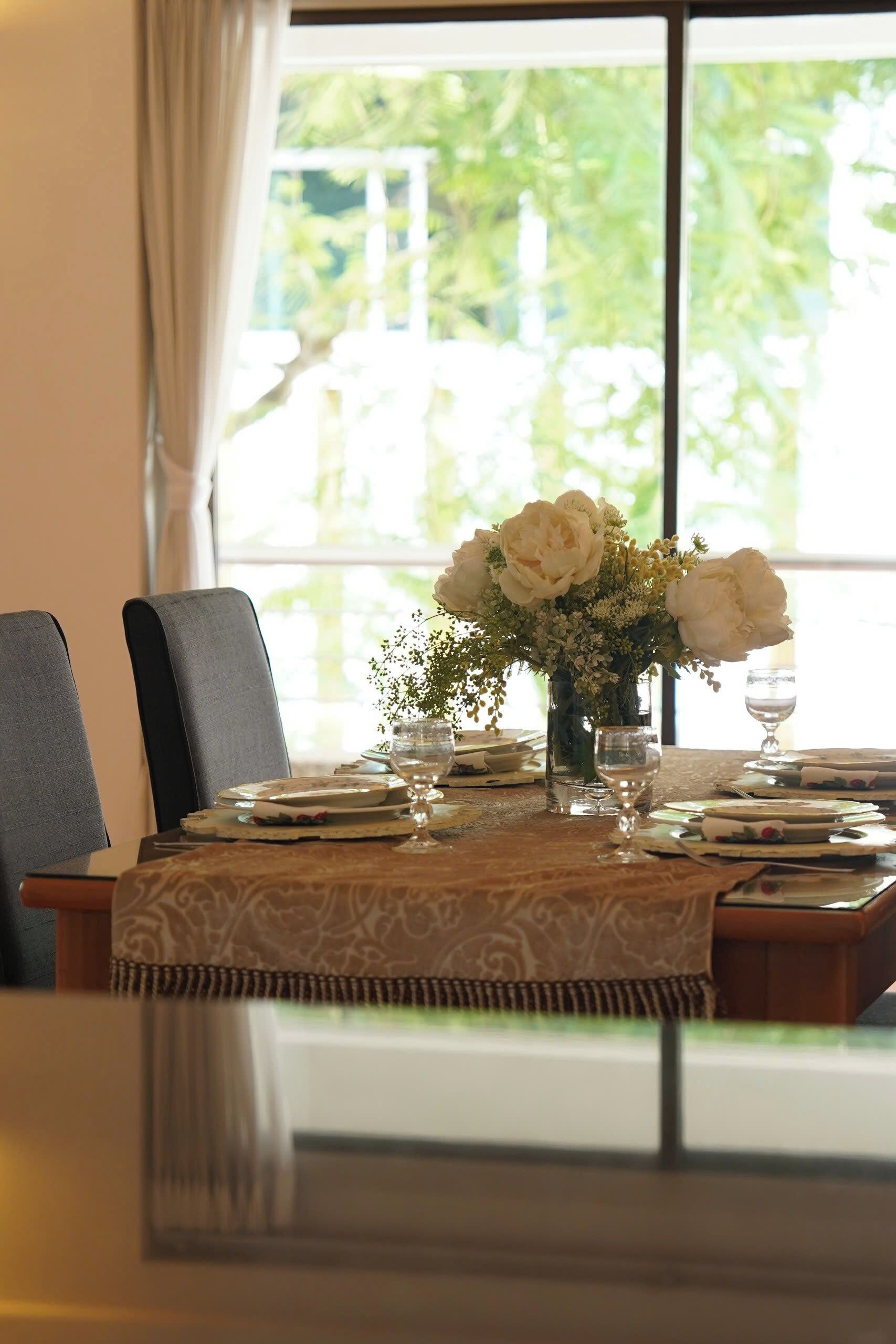 A dining table set for two with a vase of white flowers, plates, and glasses.