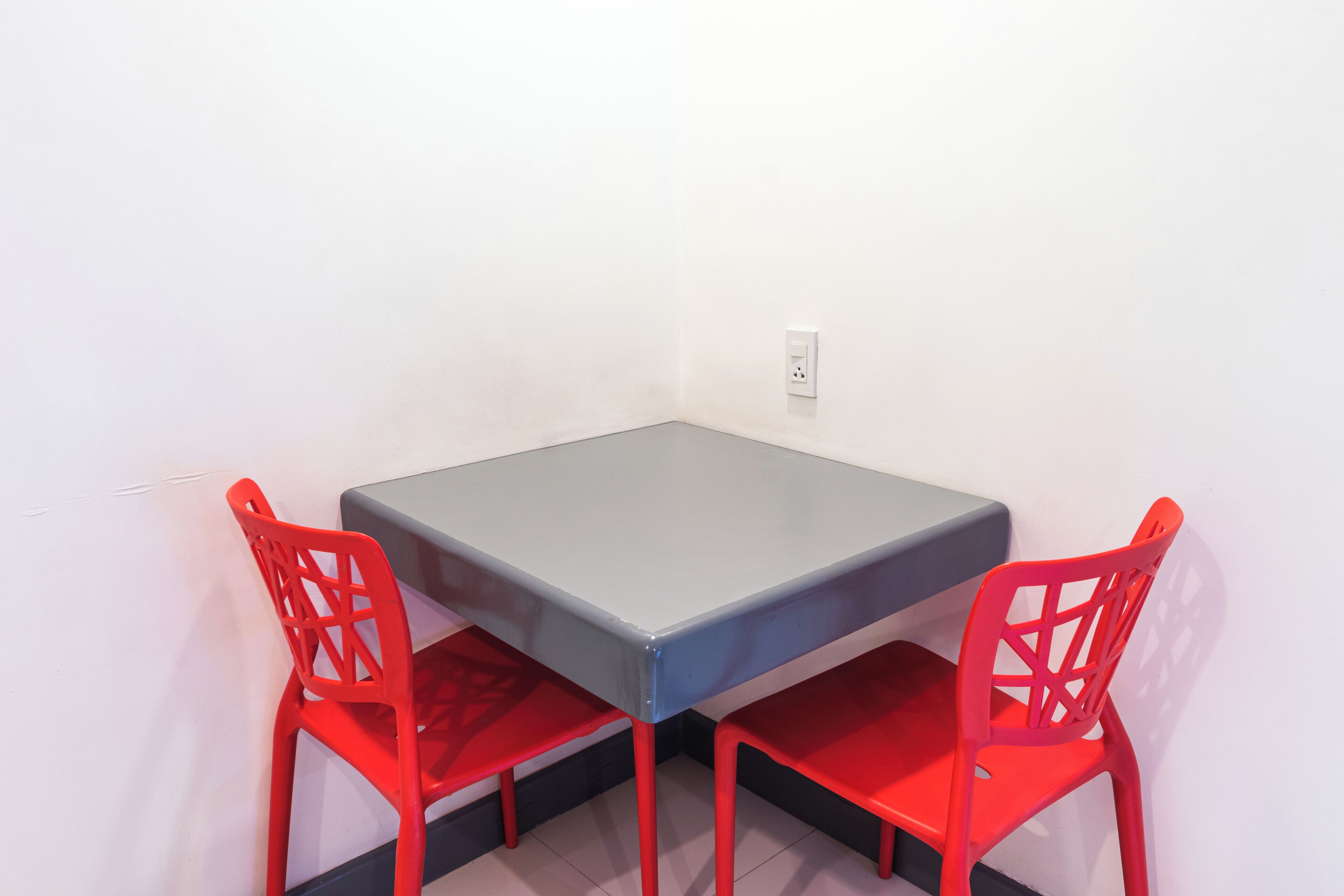 Una pequeña mesa cuadrada con dos sillas rojas.