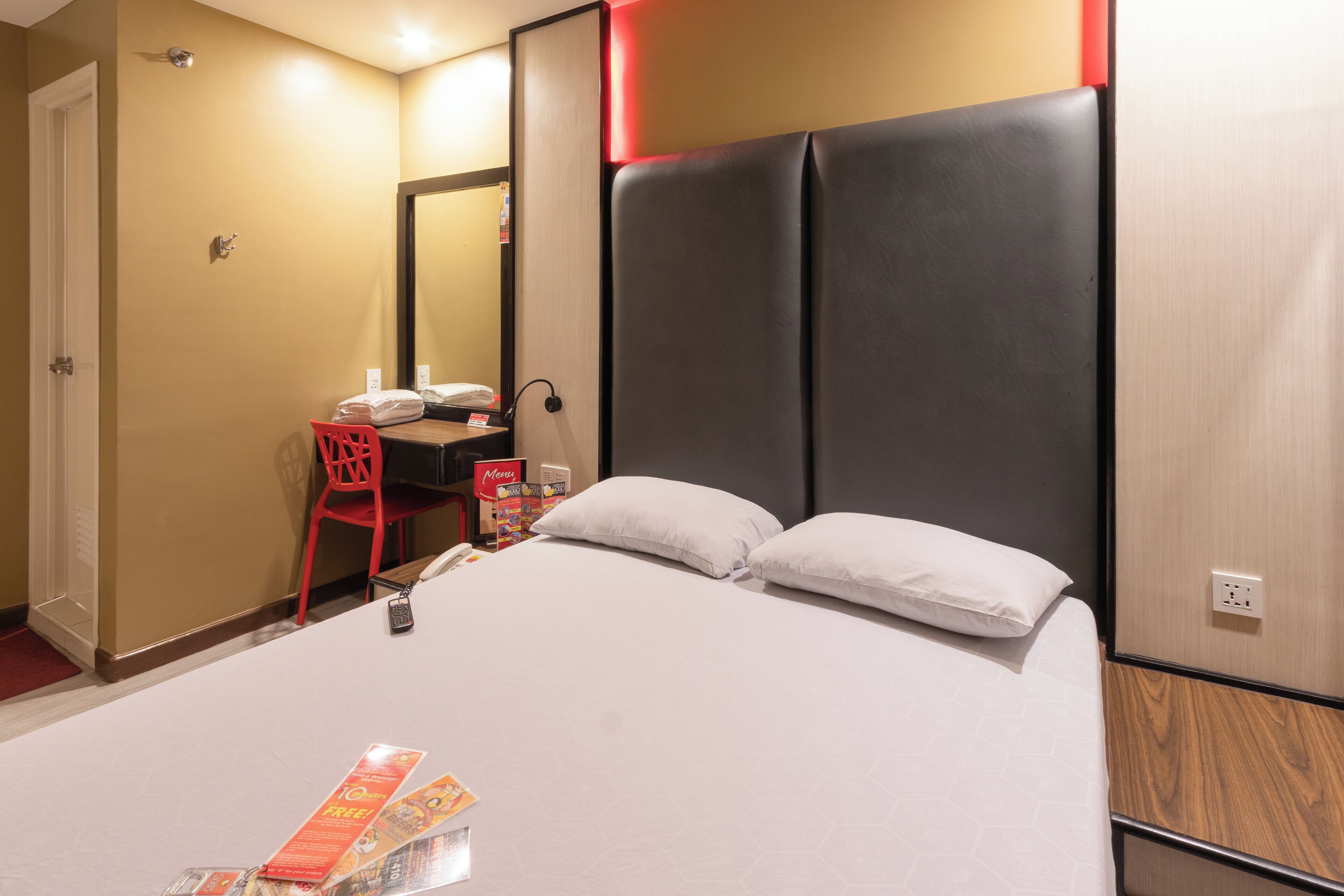 A hotel room with a large bed, a desk with a chair, a mirror, and a red chair.