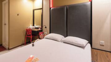 A hotel room with a large bed, a desk with a chair, a mirror, and a red chair.