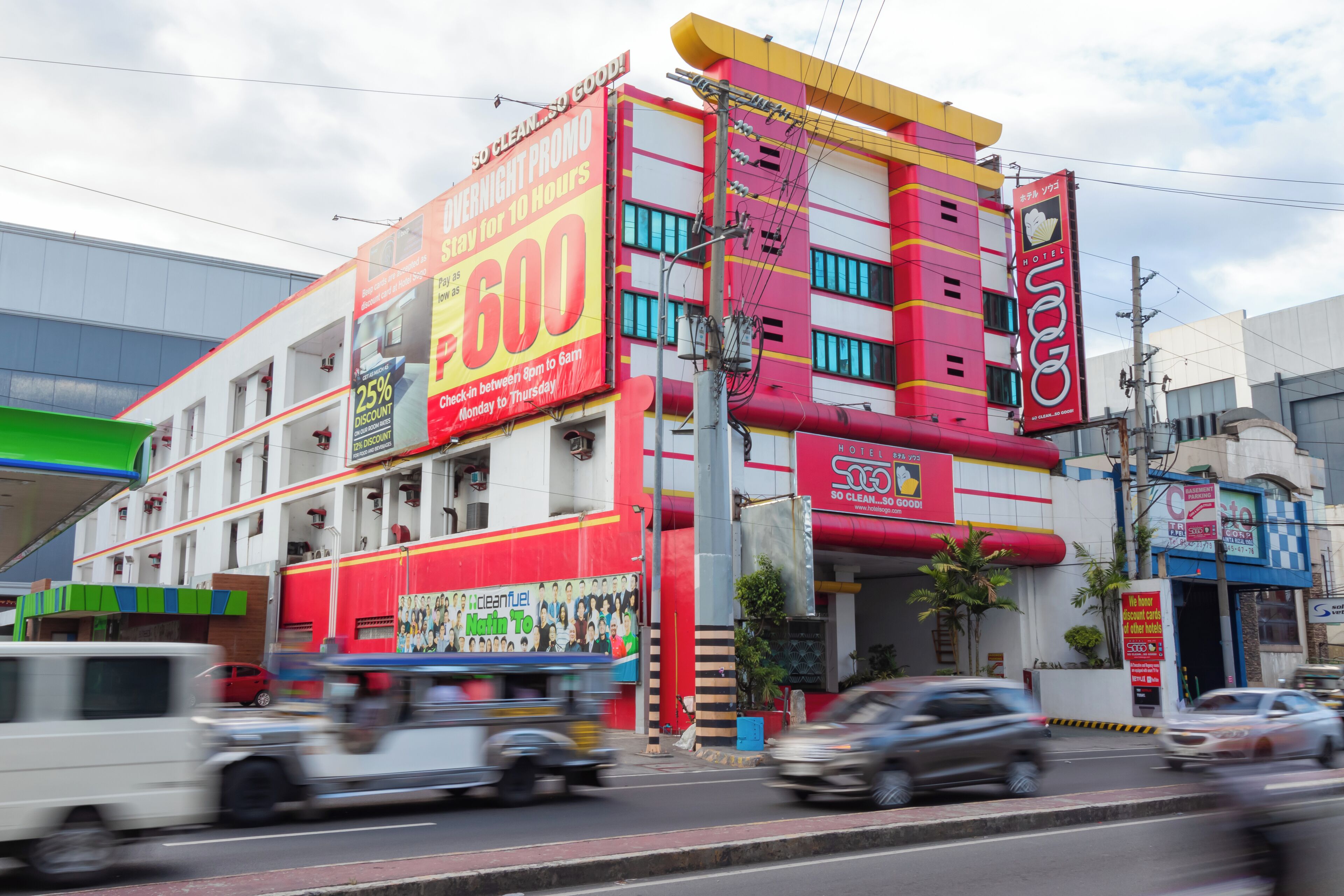 A multi-story hotel with a prominent red and yellow facade, featuring a large sign advertising a 25% discount and a 10-hour stay promotion.