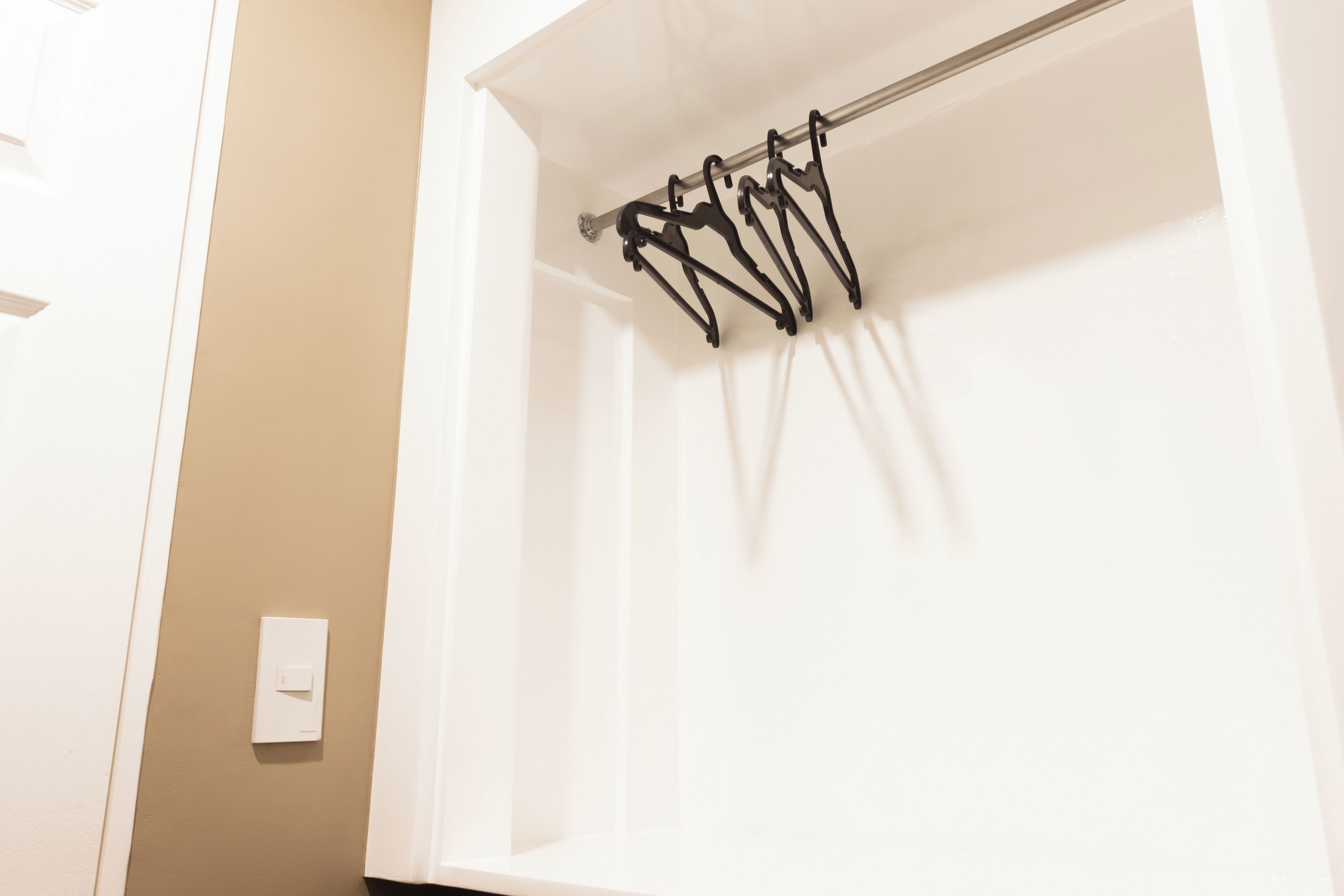 A white shower curtain rod with multiple hooks, a white wall, and a light switch.