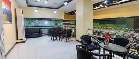 A modern restaurant with a clean, tiled floor and a mix of black and wooden furniture. There are multiple tables and chairs, and a decorative wall with a fan pattern.