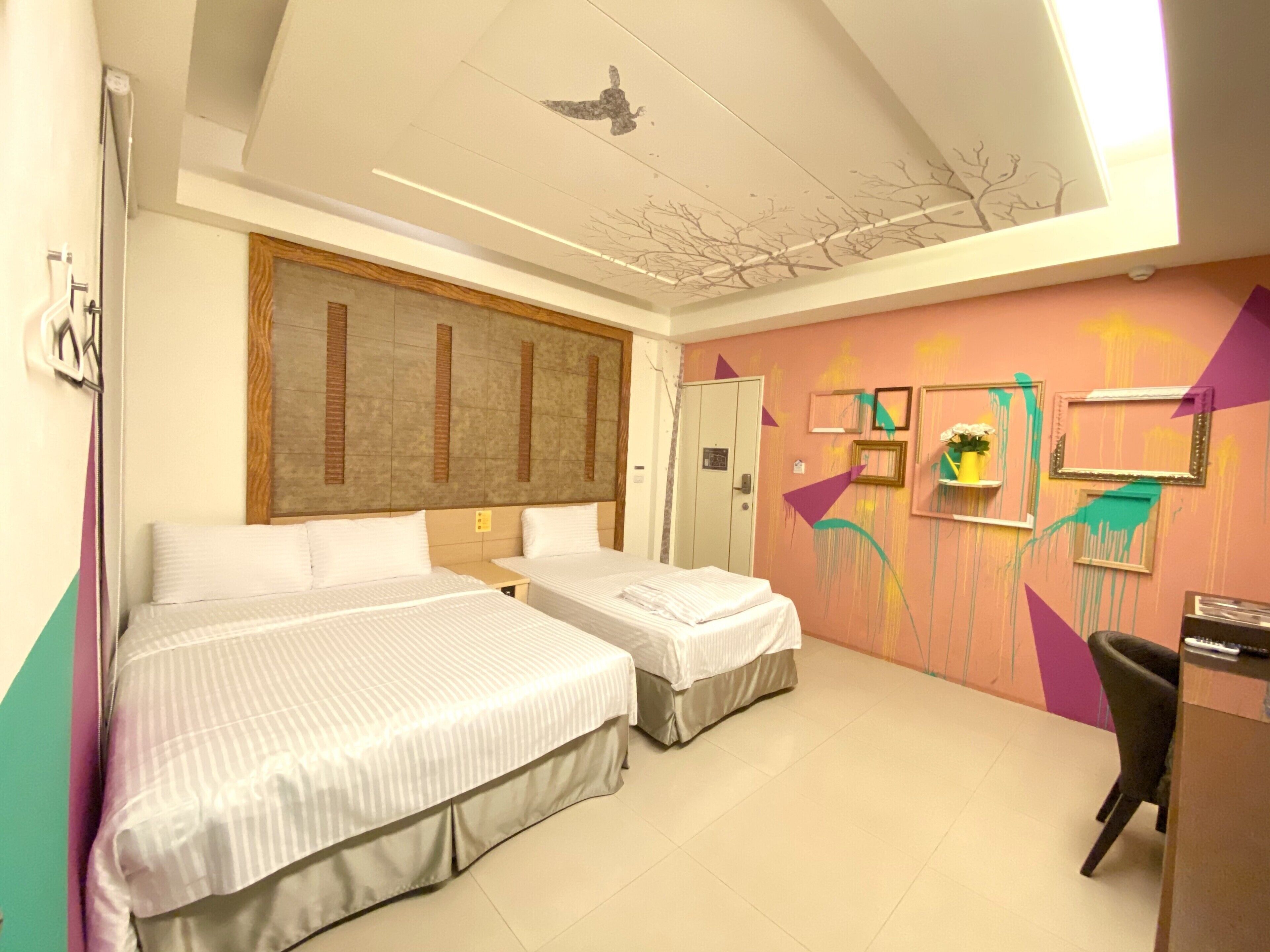 Habitación de hotel con dos camas, un escritorio y una silla. Se ve una puerta y una ventana.