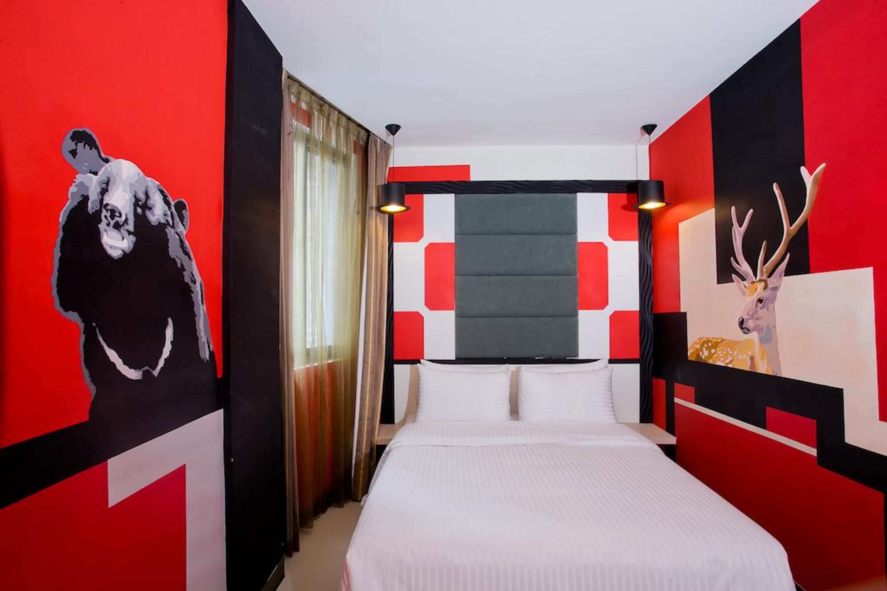 A modern hotel room with a large bed, a painting of a cow on the left wall, and a painting of a deer on the right wall.