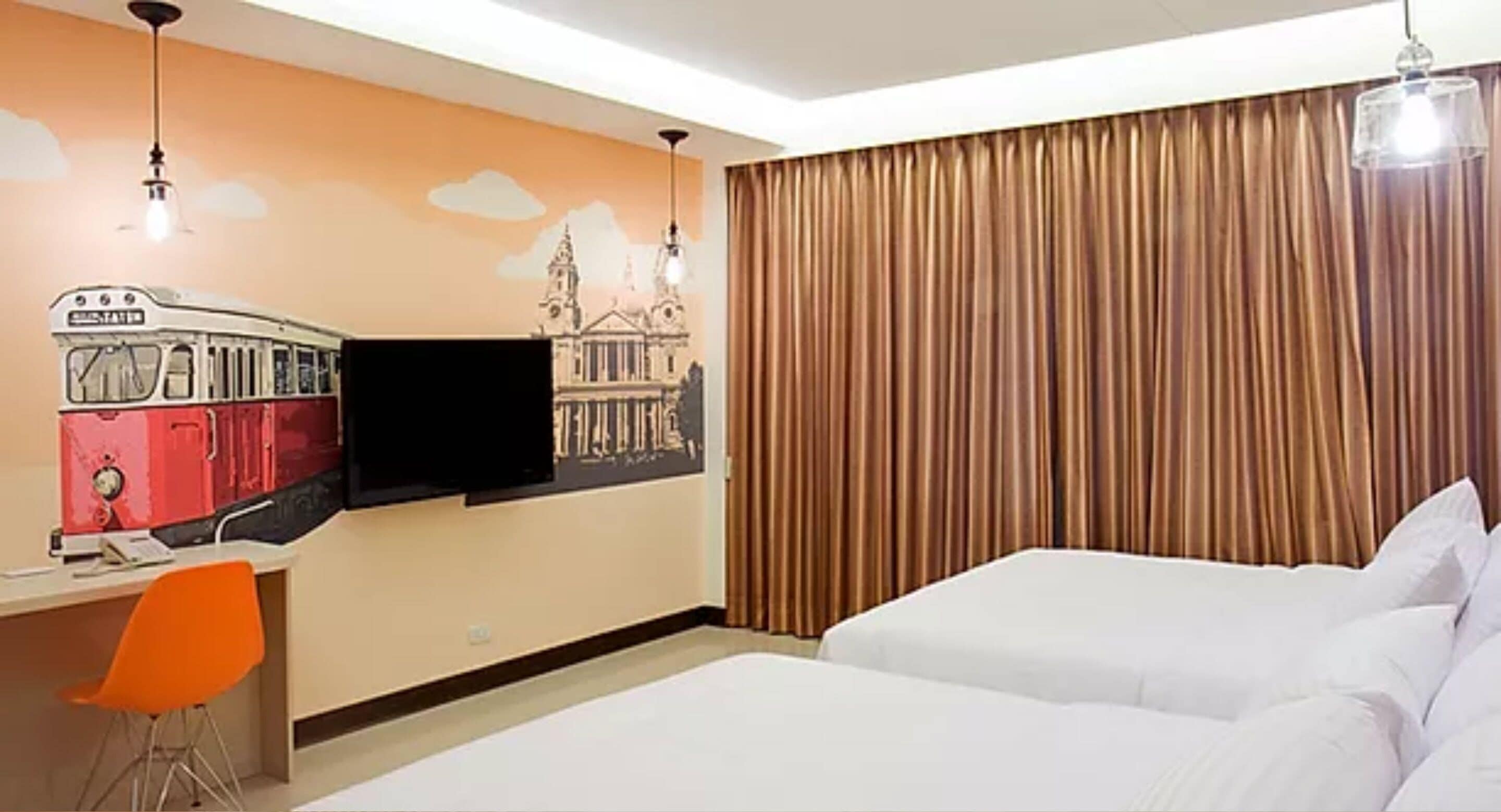 A hotel room with a bed, a desk with a chair, a flat-screen TV, and a large window with curtains.