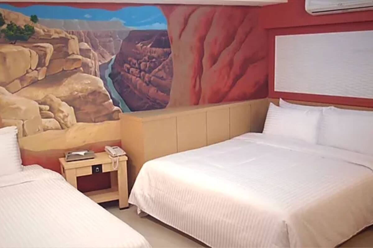 A hotel room with two beds, a mural of a canyon, and a wooden nightstand with a phone.