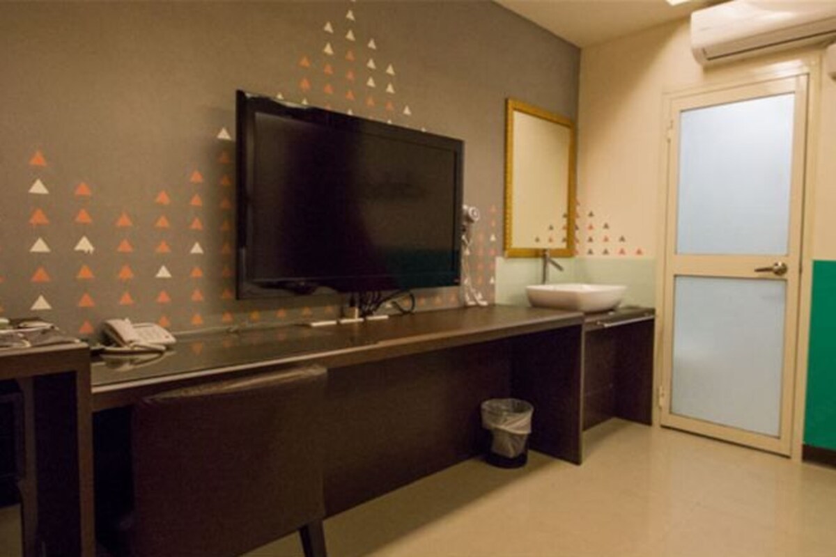 A bathroom with a large mirror, a sink, a toilet, and a television mounted on the wall.