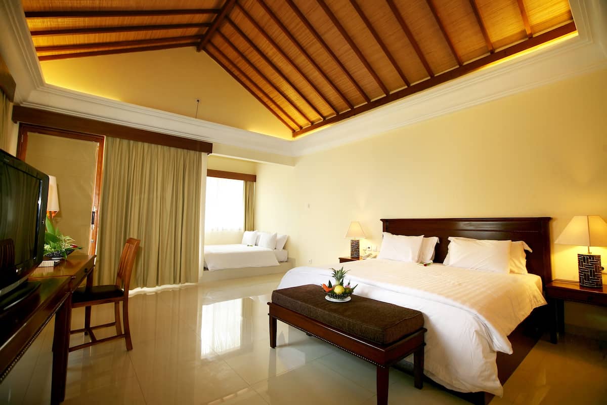 A hotel room with a large bed, a desk with a television, a chair, and a dining table with fruit on it.