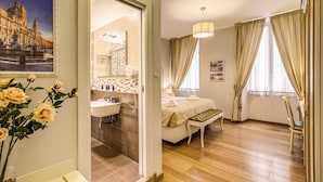 A hotel room with a bathroom, a bed, a bench, and a chair. - Gravina Suite Frattina (Rome)