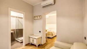 A modern hotel room with a wooden floor, a white bed, a small bedside table, and a glass-enclosed shower area. - Gravina Suite Frattina (Rome)