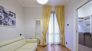 A room with a cream-colored sofa, a mirror, a framed picture on the wall, and a view through a doorway to a tiled area. - Gravina Suite Frattina (Rome)