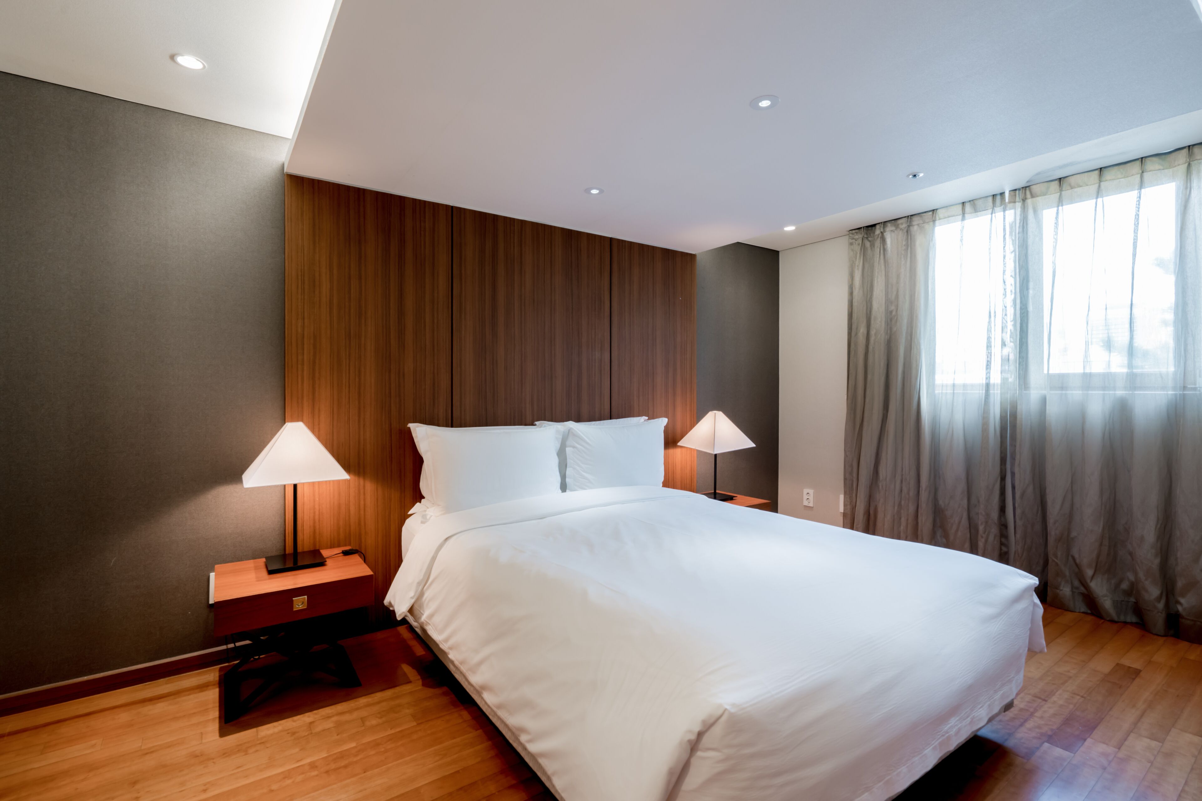 A modern hotel room with a large bed, wooden paneling on the walls, and a window with curtains.