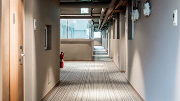 A long, narrow hallway with a striped carpet, wooden doors on the left, and a fire extinguisher in the middle.