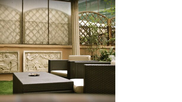 A room with wicker furniture, a small table, and a window with decorative panels. - Demi's Home (Rome)