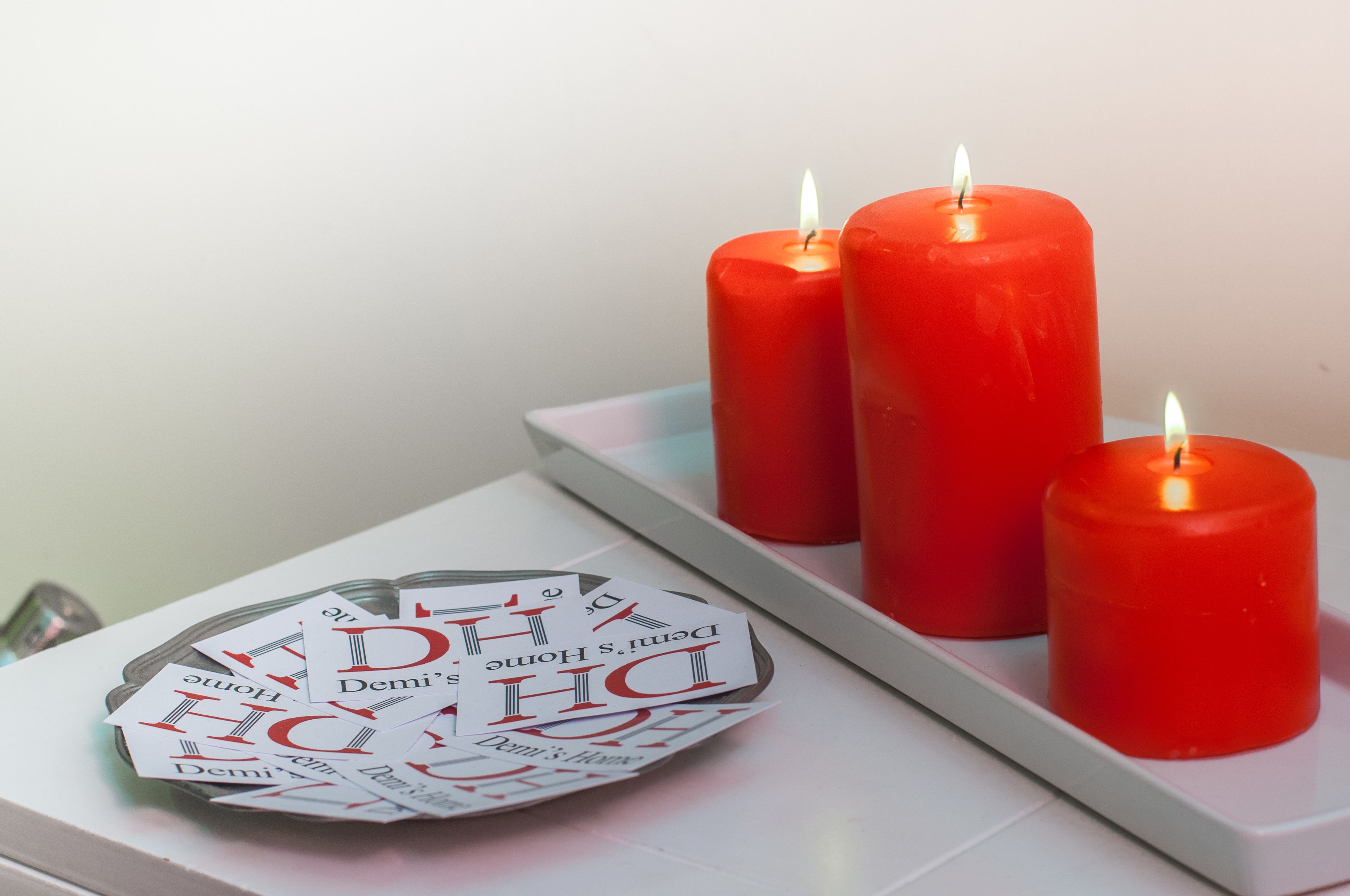 A white table with three red candles and a plate of cards with "Demi's Home" text.