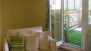 A room with a white sofa, a green and white striped pillow, and a view of a green lawn through a glass door. - Demi's Home (Rome)