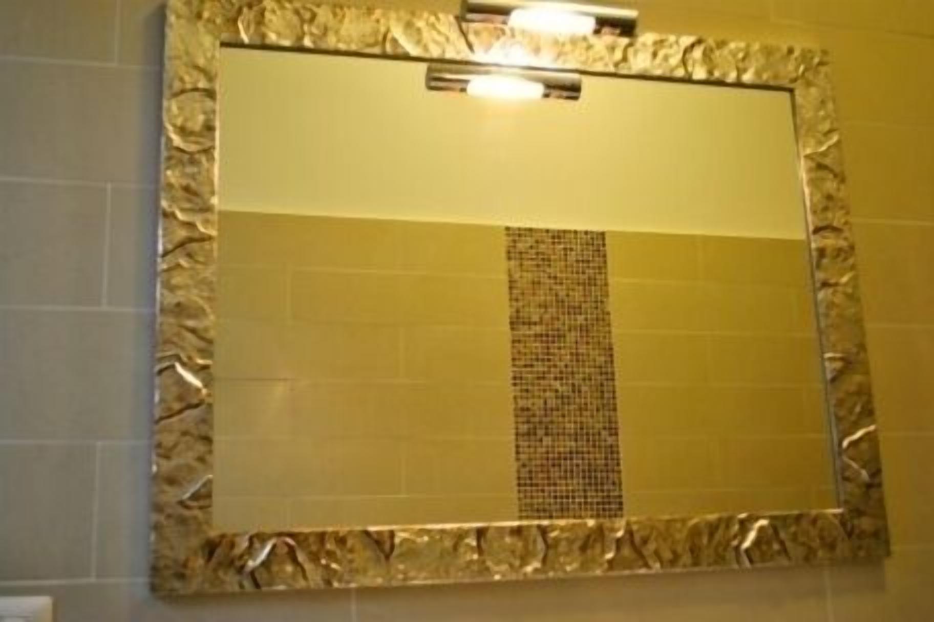 Une salle de bain dotée d’un grand miroir, d’un pare-chocs en carreaux à motifs et d’un luminaire placé au-dessus du miroir.