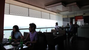 A modern dining area with large windows, wicker furniture, and a view of the sea. - Aerotel Smile Makassar (Makassar)
