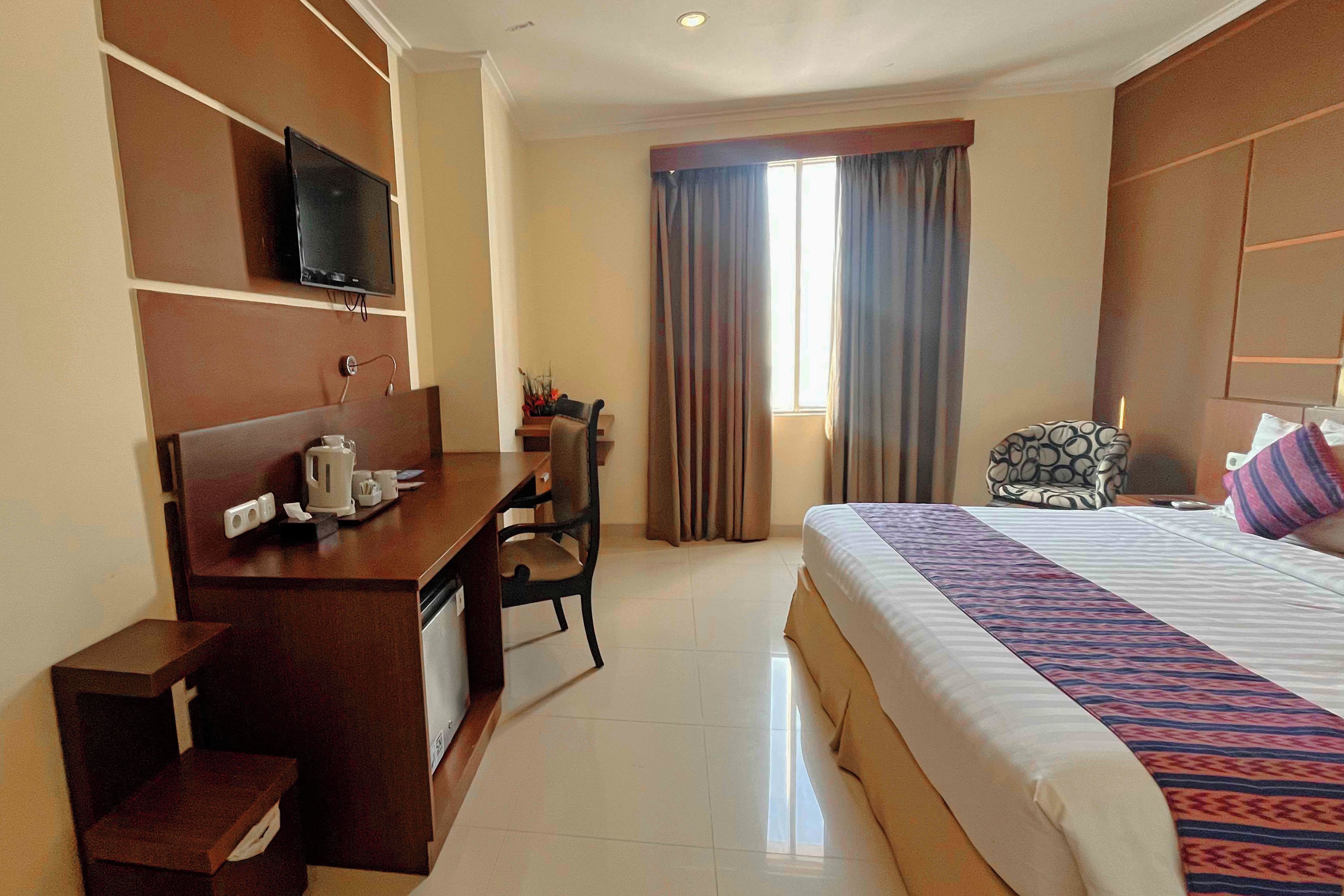 A hotel room with a bed, a desk, a chair, a television, and a window with curtains.