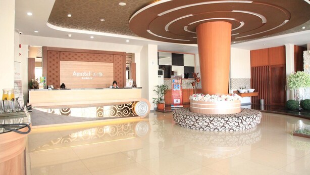 A hotel lobby with a reception desk, a central decorative column, and a patterned seating area. - Aerotel Smile Makassar (Makassar)