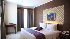 A hotel room with a large bed, a desk, a telephone, and a painting on the wall. - Aerotel Smile Makassar (Makassar)