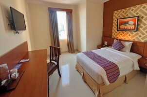 Une chambre d’hôtel avec un lit, un bureau, une chaise, une télévision et une fenêtre avec des rideaux.