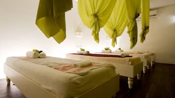 A hotel room with two beds, each with a neatly made bed, a small table with a plant, and a wall-mounted air conditioner.