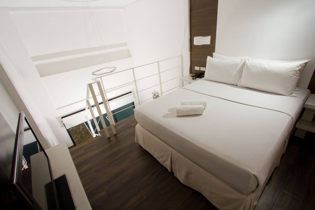 A modern hotel room with a large bed, a bedside table, a mirror, and a view of the balcony.