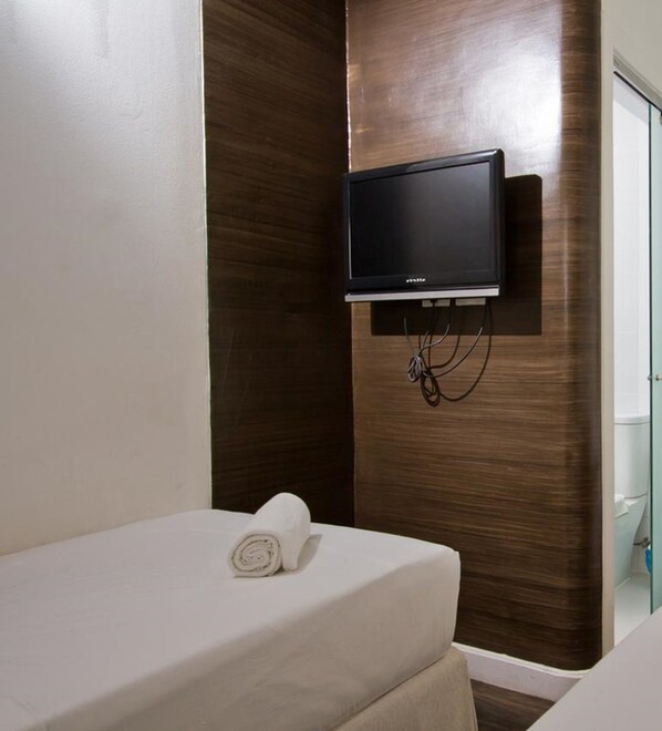 A hotel room with a bed, a wall-mounted TV, and a towel on the bed.