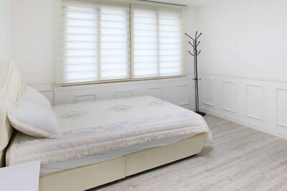 A bedroom with a bed, window blinds, a coat rack, and a ceiling light.