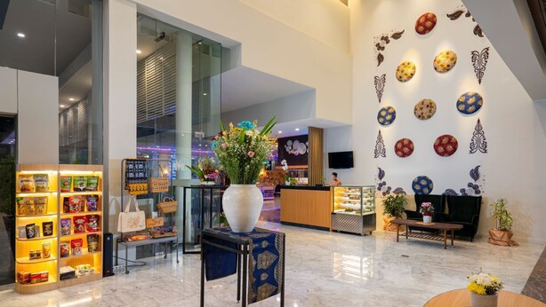 A modern hotel lobby with a reception desk, a display of snacks, a large vase with flowers, and decorative wall art. - BATIQA Hotel & Apartments Karawang (Karawang)