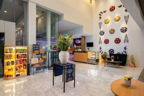 A modern hotel lobby with a reception desk, a display of snacks, a large vase with flowers, and decorative wall art. - BATIQA Hotel & Apartments Karawang (Karawang)