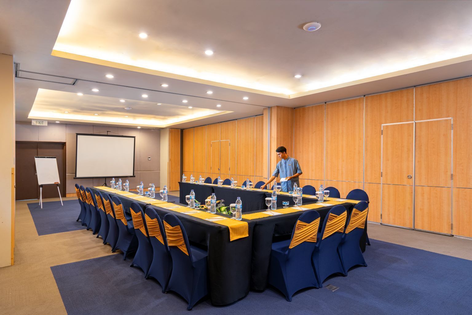 A conference room with a long table, chairs, a whiteboard, and a projector screen.