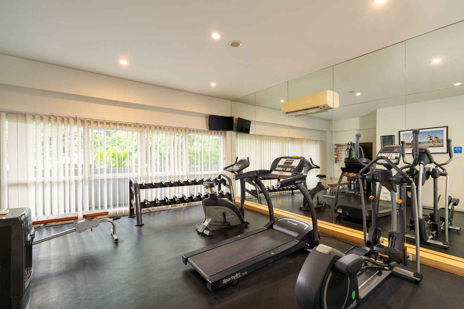 A gym with treadmills, elliptical machines, and a rack of dumbbells.