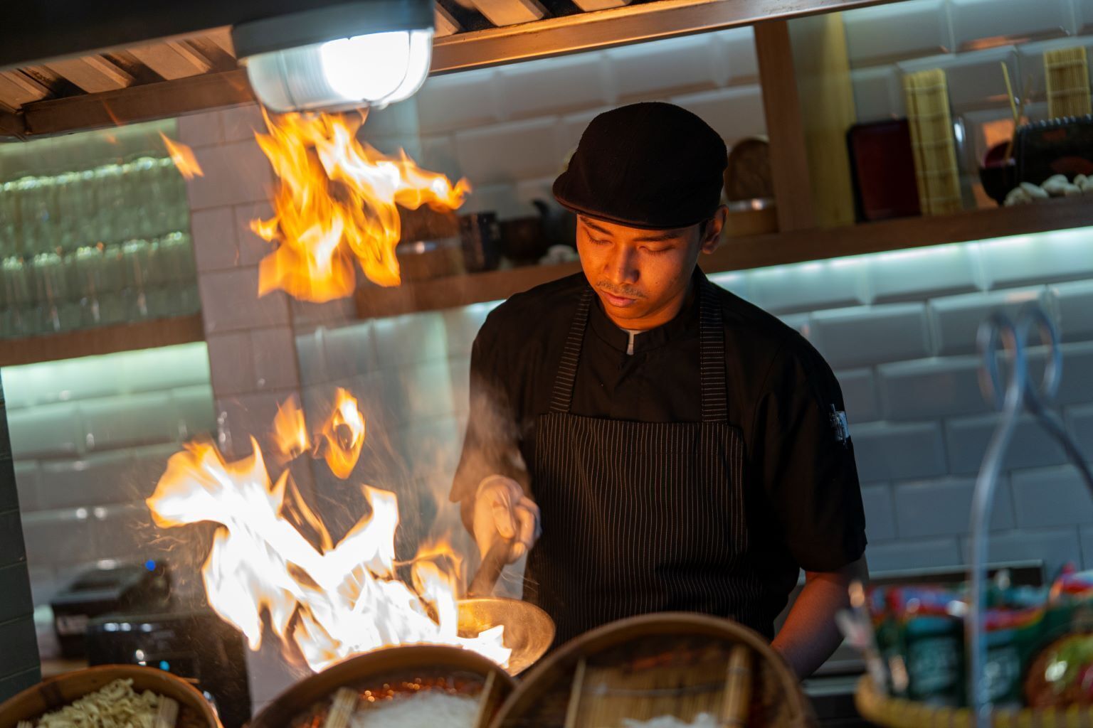 Ein Koch bereitet Essen in einer Küche zu, wobei Flammen sichtbar sind.